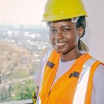Smiling female engineer wearing safety gear and hardhat at construction site.