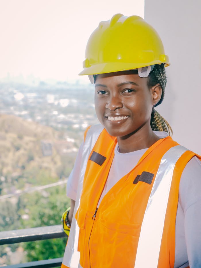 Smiling female engineer wearing safety gear and hardhat at construction site.